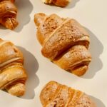 A top-down view of freshly baked croissants on a beige surface, showcasing their golden crusts.