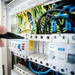 Hand of electrician working on a circuit breaker panel with colorful wires, ensuring safe electrical connections.